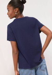 Námořnická modrá trička s krátkým rukávem a kulatým výstřihem. Lehká, texturovaná látka. V kombinaci se světle modrými džíny šortkami s bočními kapsami.