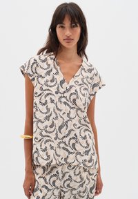 Blusa fluida realizzata in tessuto leggero, con una base color crema e modelli ondulati neri e beige. Scollatura a V e maniche a cappuccio.