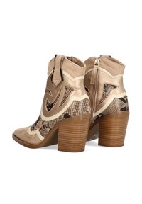 Botas tobilleras en color beige con un estampado de serpiente texturizado, un acabado metálico suave y un tacón cuadrado. Presentan una cremallera lateral y costuras decorativas.