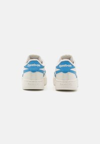 Para białych i niebieskich sneakersów Reebok pokazana od tyłu, z nazwą marki na pięcie i podeszwie na jednolitym białym tle.