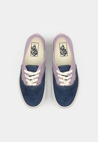 Blue suede sneakers with a lavender fabric collar, white laces, and a rubber sole, featuring a logo on the insole and a double-stitched design.