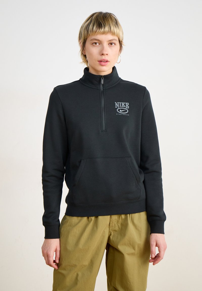 Sudadera negra con cremallera y cuello alto, bolsillo delantero y logo blanco de Nike en el pecho. Confeccionada en un tejido suave con puños de canalé.
