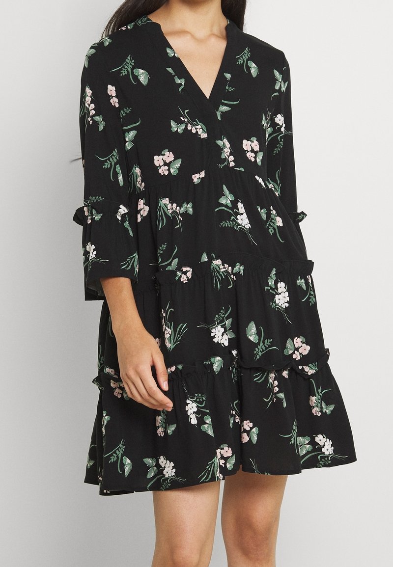 Robe noire à volants avec manches trois-quarts, ornée de motifs floraux roses et blancs ainsi que de papillons verts.