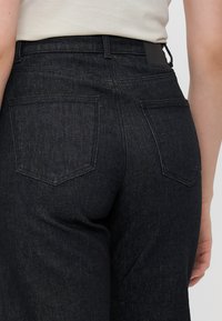 Black denim jeans featuring straight legs, five pockets, tonal stitching, and a classic waistband with a back patch.