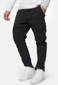 Schwarze Cargo-Hosen mit mehreren Seitentaschen, geradem Schnitt und strapazierfähiger Textur. Tragen mit weißen Sneakers, was einen lässigen Stil zeigt.
