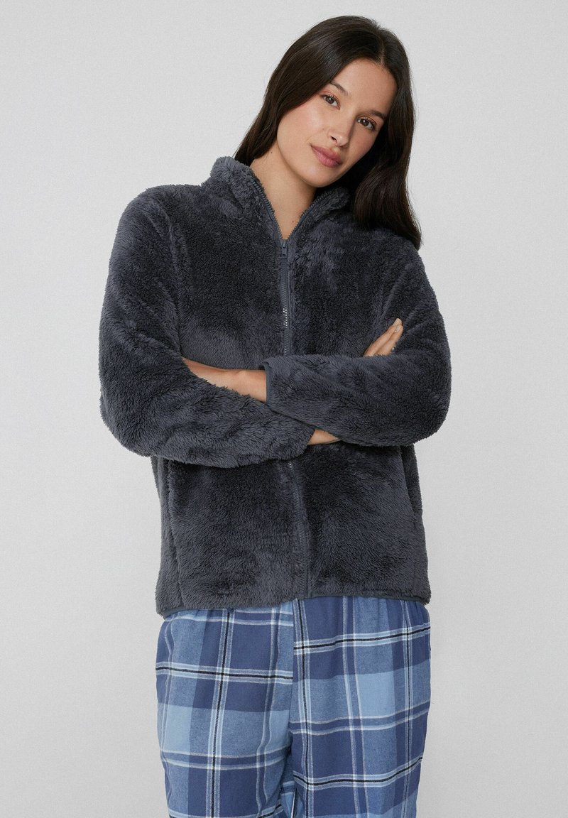 Chaqueta de forro polar gris oscuro, con cremallera y capucha; textura suave. Combinada con pantalones a cuadros azules que presentan cuadrados claros y oscuros.