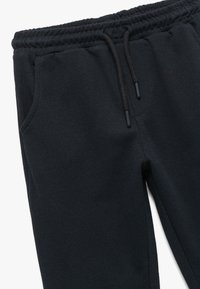 Schwarze Jogginghosen mit elastischem Bund, Kordelzug und seitlichen Taschen. Der Stoff hat eine strukturierte Oberfläche, die Langlebigkeit und Komfort zeigt.