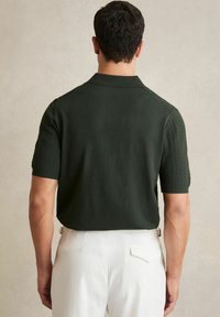 Polo de culoare verde închis cu mânecă scurtă, cu accente texturate pe umeri, conceput cu un guler clasic și o croială lejeră.