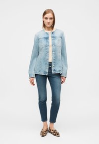 Veste en denim bleu clair avec une fermeture à boutons, deux poches poitrine et des manches longues, associée à un jean skinny foncé et des chaussures à imprimé léopard.