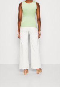 Ljusgrön ärmlös topp i kombination med vita vida byxor. Byxorna har bakfickor och en lätt struktur, kompletterade med beige klacksandaler.