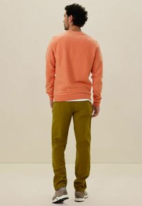 Koraal fleece sweatshirt met ribbelboorden, gecombineerd met olijfgroene broek, aangevuld met grijze en witte sneakers. Effen achtergrond.
