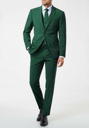Costume trois pièces vert en tissu lisse ; présente une coupe ajustée, des revers crantés et des chaussures noires. Les accents comprennent un gilet et une cravate.