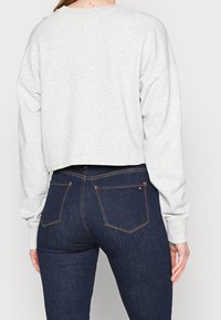 Lichtgrijze cropped sweatshirt met lange mouwen, ronde hals en zachte textuur, gecombineerd met donkerblauwe spijkerbroek met contrasterende stiksels en vier zakken.