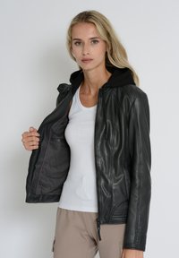 Schwarze Lederjacke mit Kapuze, Reißverschluss und gerippten Details an den Ärmeln. Das Innere verfügt über ein glattes Futter mit lila Akzenten.