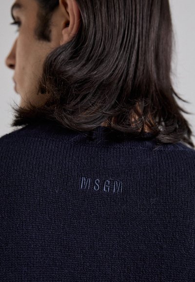 Pulover tricotat bleumarin, cu un gât ribilat și un logo brodat subtil "MSG" pe spate, aproape de guler.