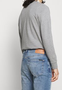 Szara koszula z długim rękawem w połączeniu z jasnoniebieskimi dżinsami z denimu z naszywką ze skóry marki Calvin Klein Jeans na tylnym pasku.