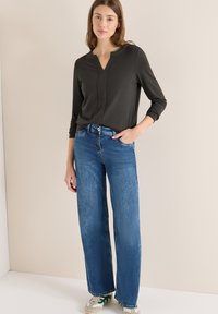 Tummanharmaa pitkähihaisen V-kaula-aukkoinen paita, yhdistetty leveälahkeisiin sinisiin farkkuihin, joissa on klassinen viiden taskun muotoilu ja rento istuvuus.