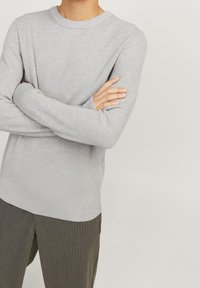 Chemise à manches longues gris clair côtelée avec un col rond et des poignets ajustés, associée à un pantalon rayé vert foncé.