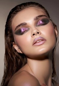 Modell med langt, vått brunt hår; har dristig svart og lilla øyensminke og en lys rosa glanslepp. Glatt hud med en subtil glød.