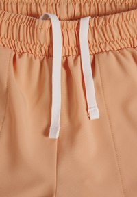 Pfirsichfarbene Joggingkurzshorts mit einem elastischen Bund und weißen Kordeln. Hergestellt aus weichem, glattem Stoff mit dezenten Nähdetails.