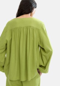 Zielona lniana bluzka z długimi rękawami, z tyłem w stylu marszczonym. Miękka tekstura, luźny krój, zaokrąglony dół i okrągły dekolt.