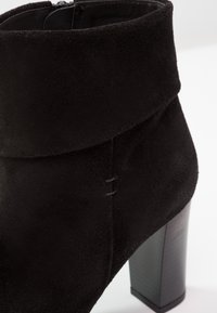 Bottine noire en daim avec revers plié et talon bloc, avec une couture latérale visible et une fermeture éclair.