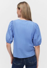 Blårandig blus med puffade korta ärmar, rundad halsringning och avslappnad passform. Tyget har en slät textur med en subtil glans.