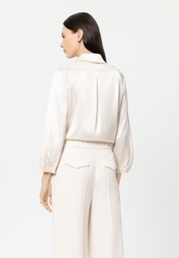 Silk beige blouse with a collar, gathered sleeves, and a subtle pleat at the back, paired with matching wide-leg trousers.