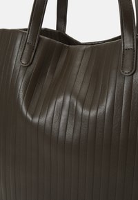 Sac fourre-tout en cuir vert foncé avec une texture à rainures verticales, deux poignées solides et un bord supérieur doux et courbé. L'intérieur est visible.