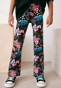 Svarta grafiska utsvängda byxor med färgglada mönster av blommor, moln, fredssymboler och text i rosa, blått och gult; i bomullsmaterial.