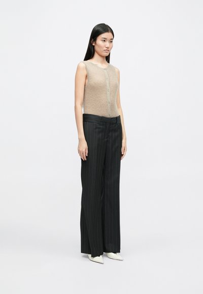 Beige ilma varrukatega topp, millel on nupuga sulgemine, kombineeritud kõrge vöökohaga mustade triibuliste pükstega ja teravatipuliste valgete kontsadega.