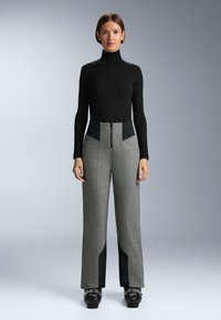 Sivé vzorované nohavice s vysokým pásom, tmavozelené bočné panely a detail so zipsom. Kombinované s čiernym rolákom s dlhým rukávom.