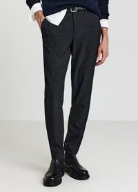 Pantaloni grigio scuro con motivo testurizzato, vestibilità slim e tasche laterali. Abbinati a stivaletti neri e maglione blu navy.