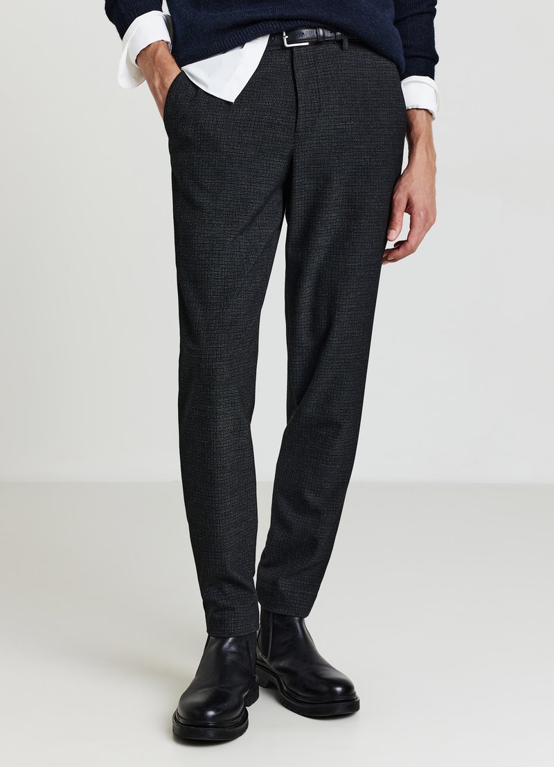 Pantaloni grigio scuro con motivo testurizzato, vestibilità slim e tasche laterali. Abbinati a stivaletti neri e maglione blu navy.