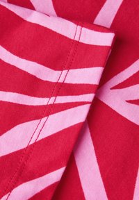 Rød stof med kraftige, vinkelløse pink striber. Teksturen er glat med synlige stikninger langs kanterne.
