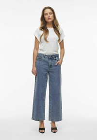 Camiseta gris claro de manga corta combinada con jeans de denim azul de pierna ancha y cintura alta. Sandalias negras de tacón completan el look.