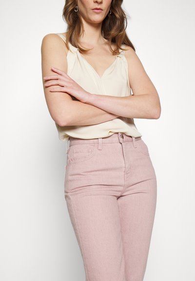 Top sem mangas de cor creme com detalhe em nó, combinado com jeans de cintura alta em rosa claro, com bolsos frontais e fecho de botão.