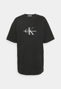 Černé oversized tričko z bavlny s bílým logem "Calvin Klein Jeans" a velkým "K" na hrudi. Krátké rukávy a kulatý výstřih.