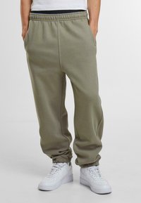 Pantaloni de trening verde măsliniu, confecționați dintr-un material moale, având un elastic în talie și la glezne, cu buzunare laterale și o croială relaxată.