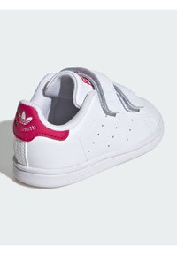 White leather sneaker with pink heel tab and grey velcro straps. Features perforations on the sides and a textured white rubber sole.