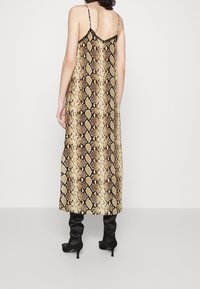 Dyreprint maxi kjole i guld- og sort nuancer, med tynde stropper og en let silhuet, parret med knæhøje sorte støvler.