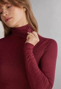 Burgundský rolák vyrobený z měkké, texturované tkaniny, s dlouhými rukávy a jemnými detaily kolem límce.