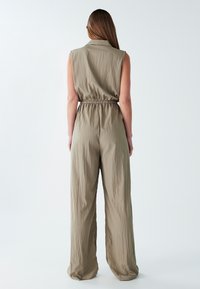 Khaki overal bez rukávů, s nařaseným pasem a širokými nohavicemi vyrobenými z lehké strukturované tkaniny.