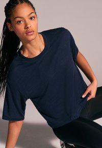 Navy blue short-sleeve athletic t-shirt with a relaxed fit, round neckline, and textured fabric, styled with black leggings.
