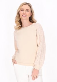 Felpa beige chiaro con maniche leggere, in pizzo a fantasia. Presenta una vestibilità rilassata e polsini a coste. Texture liscia e morbida in tutto il capo.