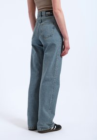 Light blue denim jeans with a high waist, wide-leg fit, two back pockets, and a black brand label on the waistband.