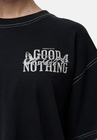 Czarny bawełniany t-shirt z białym nadrukiem "PRESENTED BY GOOD FOR NOTHING" oraz grafikami motyli, z kontrastowym stęgnowaniem wzdłuż dekoltu.