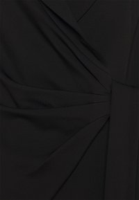 Tissu noir avec des plis détaillés rassemblés à une ceinture, créant des plis structurés et une apparence lisse et ajustée.