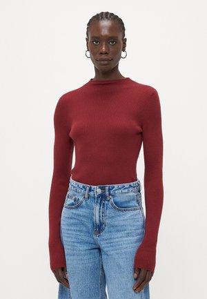 Ribbede strikket langermet topp i mørkerød, med høy hals og lange ermer, kombinert med lys blå høytlivsjeans.