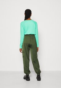 Długi rękaw, miętowa bluzka z teksturowanym wzorem w połączeniu z oliwkowymi spodniami cargo z elastycznym pasem i bocznymi kieszeniami.